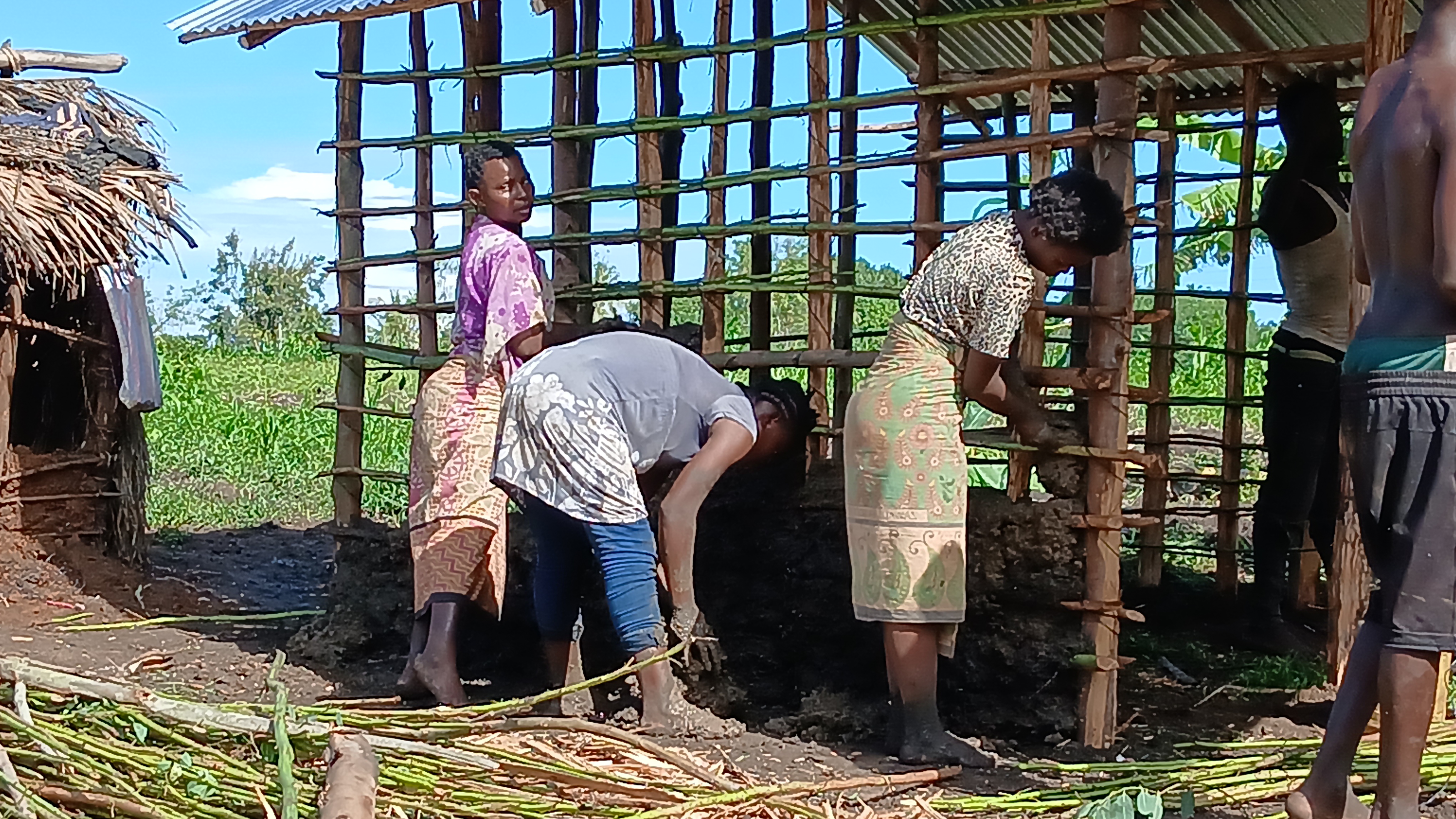 mama na watoto wake wakifanya bidii kukandika nyumba.